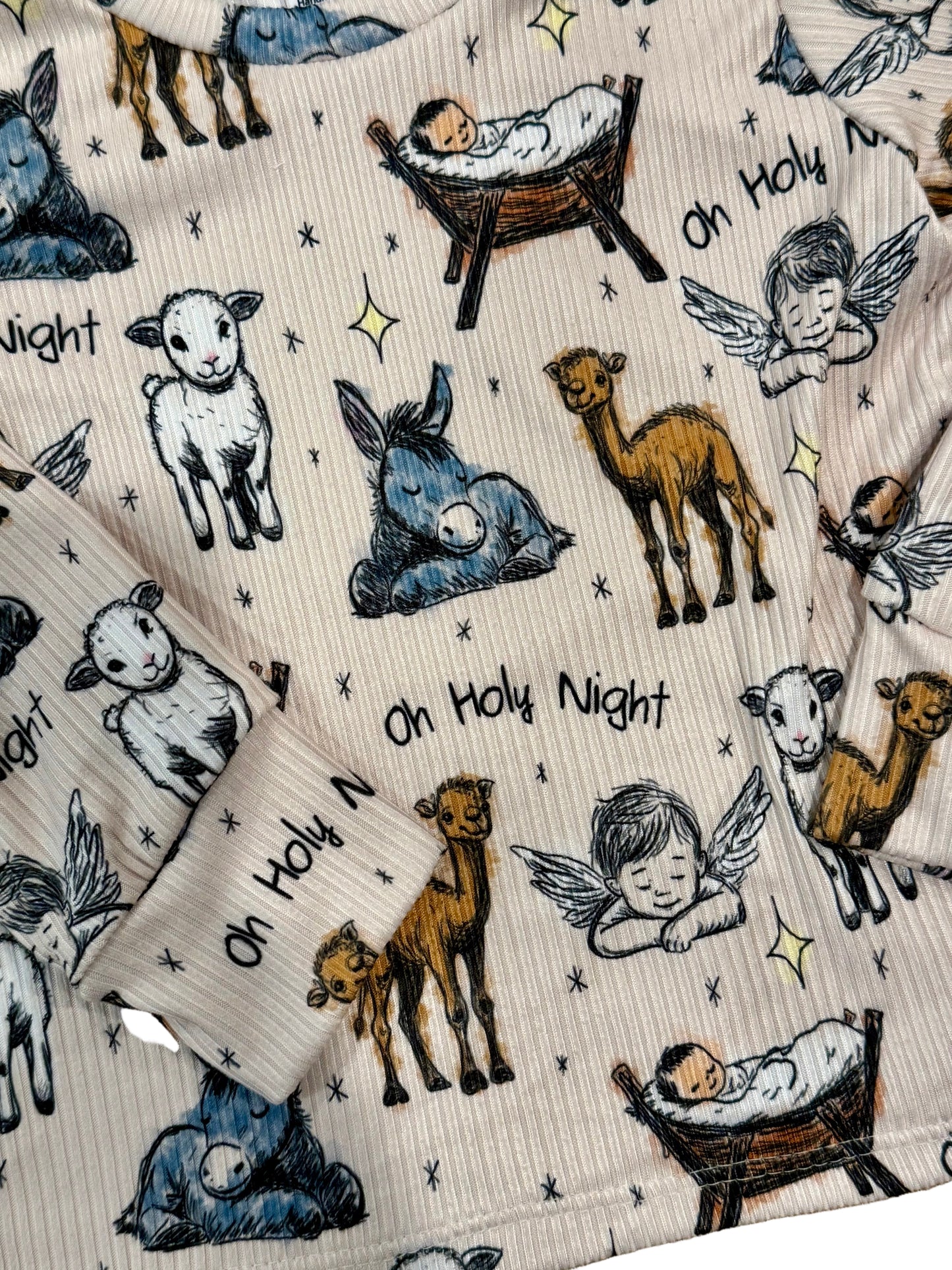 Pajamas with nativity scene design featuring baby Jesus, sheep, donkeys, and angels on a beige background.