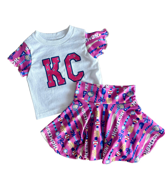 Children's outfit with white shirt and pink shorts featuring 'KC' on a textured surface