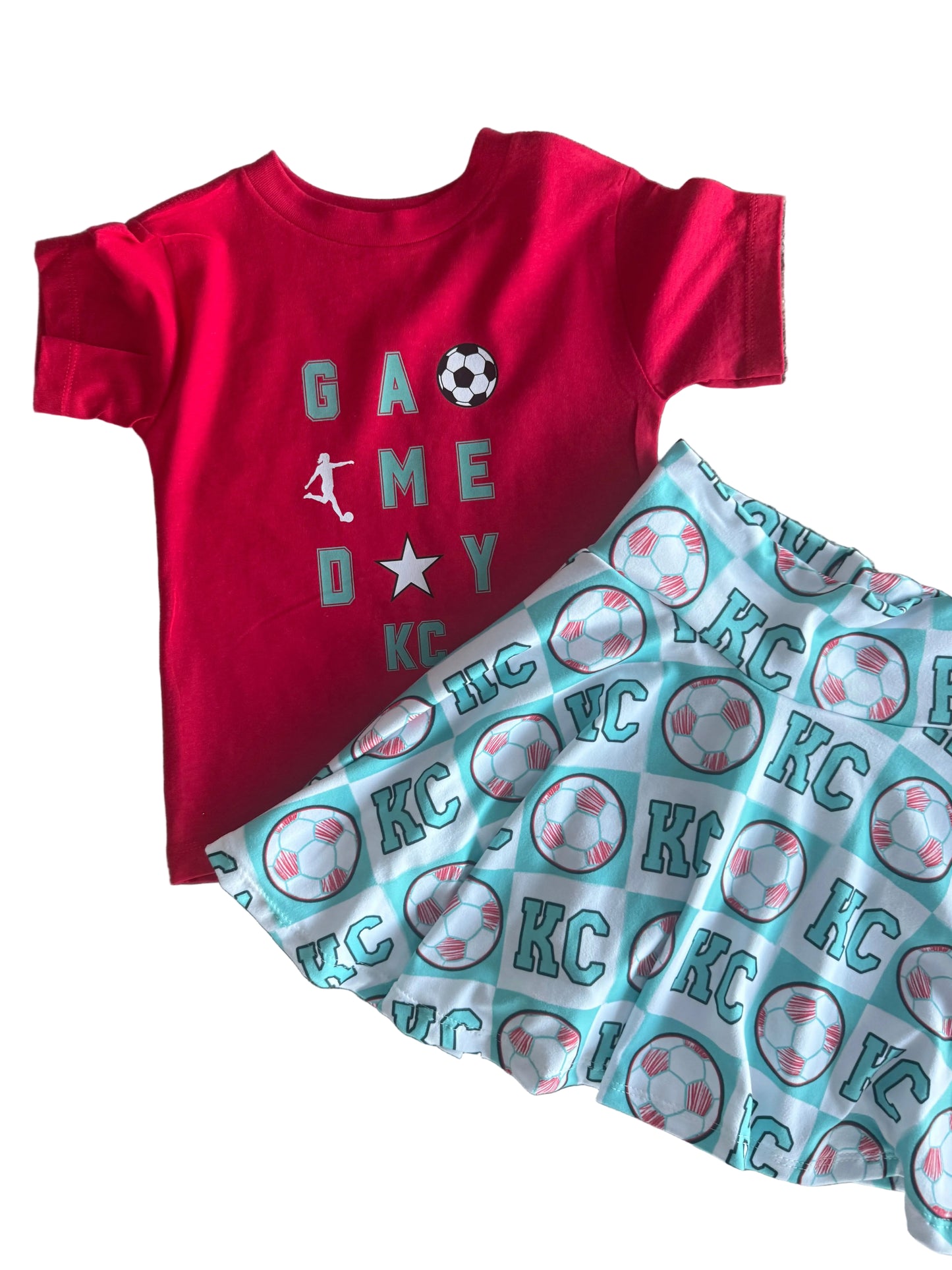Red shirt with 'Game Day' text and a white baby blanket with 'KC' pattern on a white surface