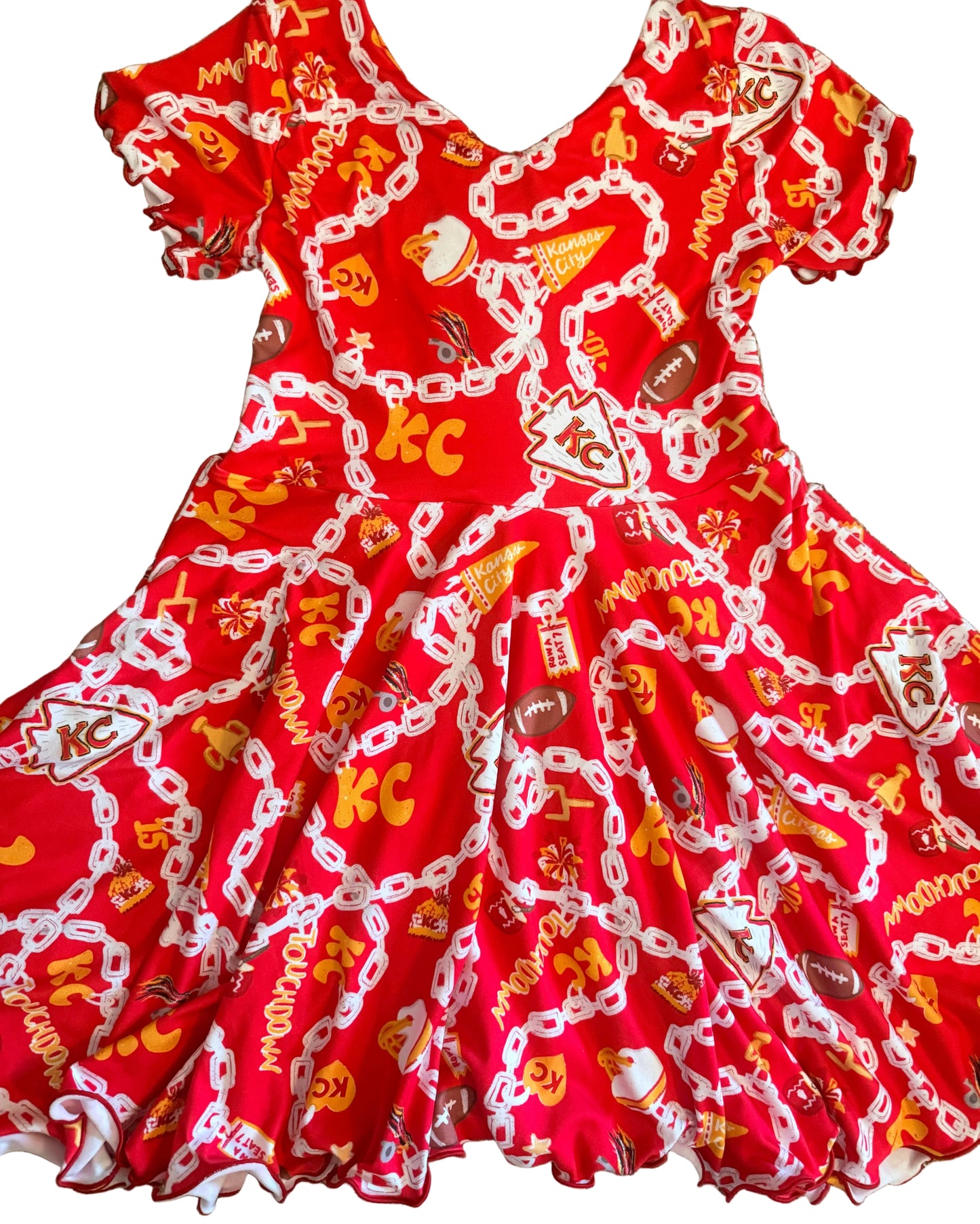 A red ruffled dress  laid flat on white floor featuring a white chain pattern with football and KC graphics
