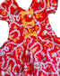 A red fabric dress with a football-themed print featuring white chain graphics, orange and yellow details, and three yellow bow accents at the center, laid flat on white carpet.