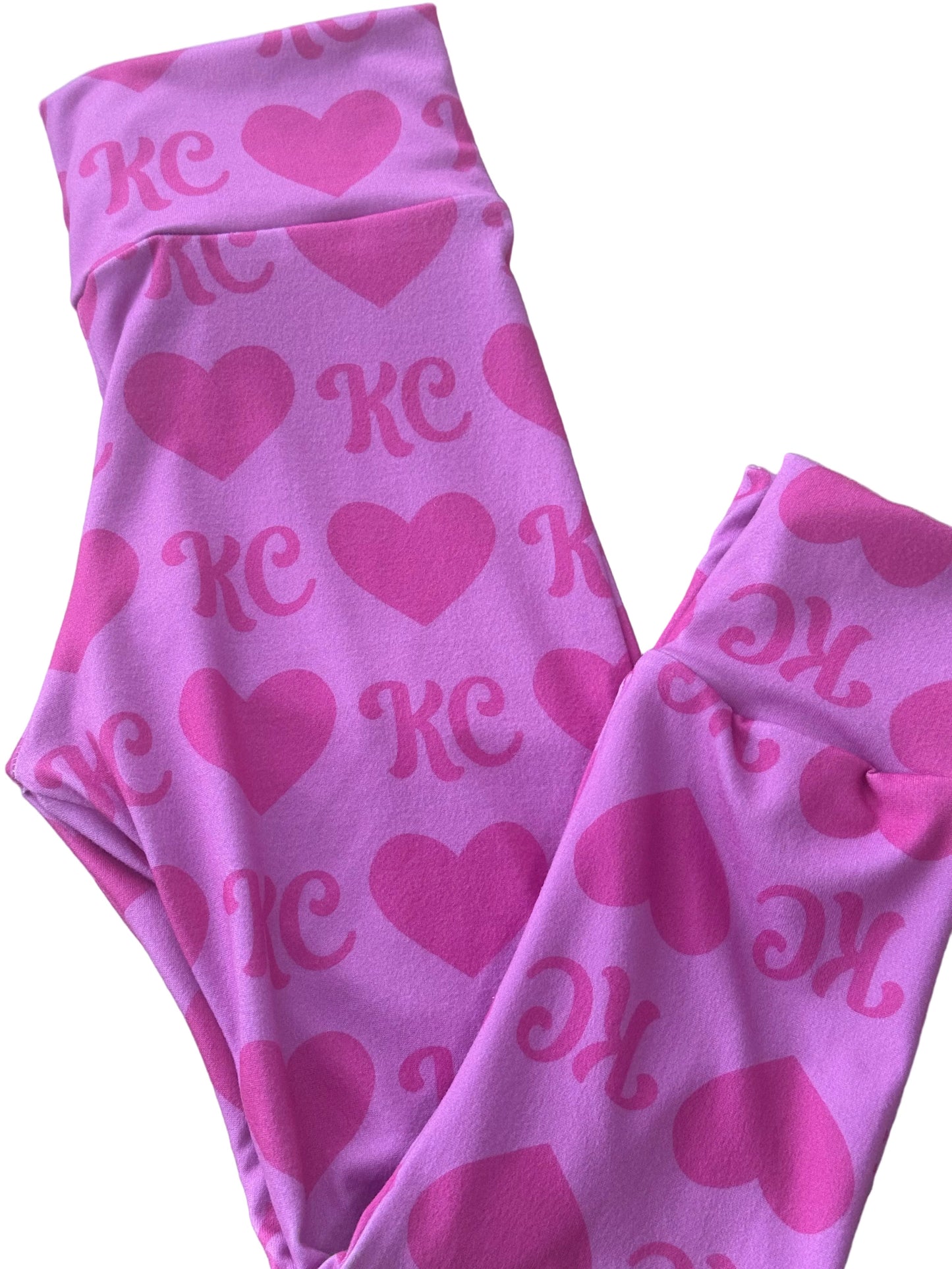 Pink fabric with heart and 'KC' pattern on a light wooden surface