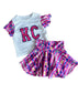 Children's outfit with white shirt and pink shorts featuring 'KC' on a textured surface