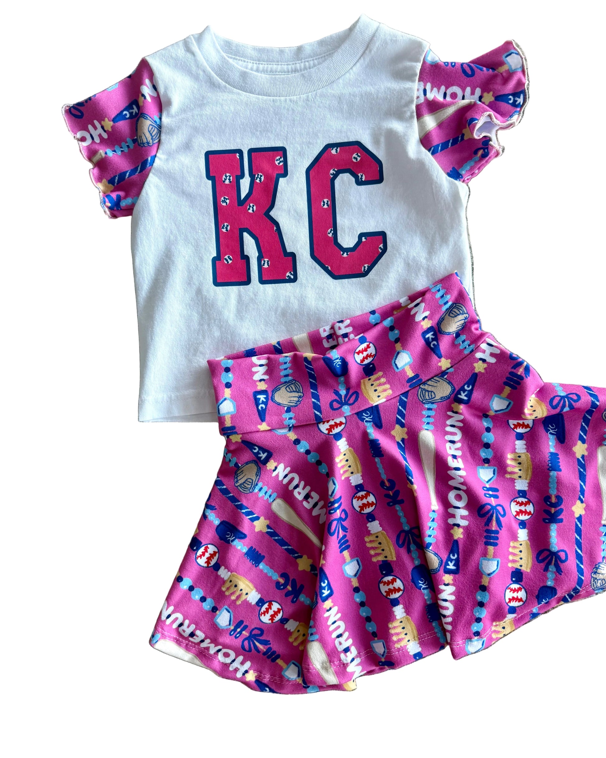 Children's outfit with 'KC' shirt and pink shorts on a textured surface