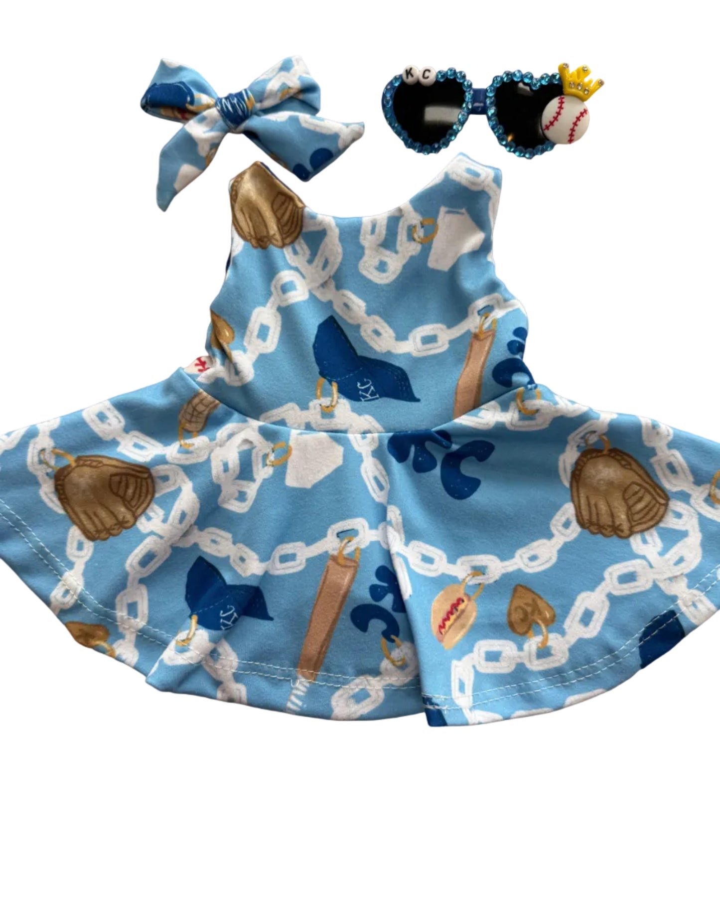 Children's blue dress with sports-themed print on a wooden surface, accompanied by a headband and sunglasses.