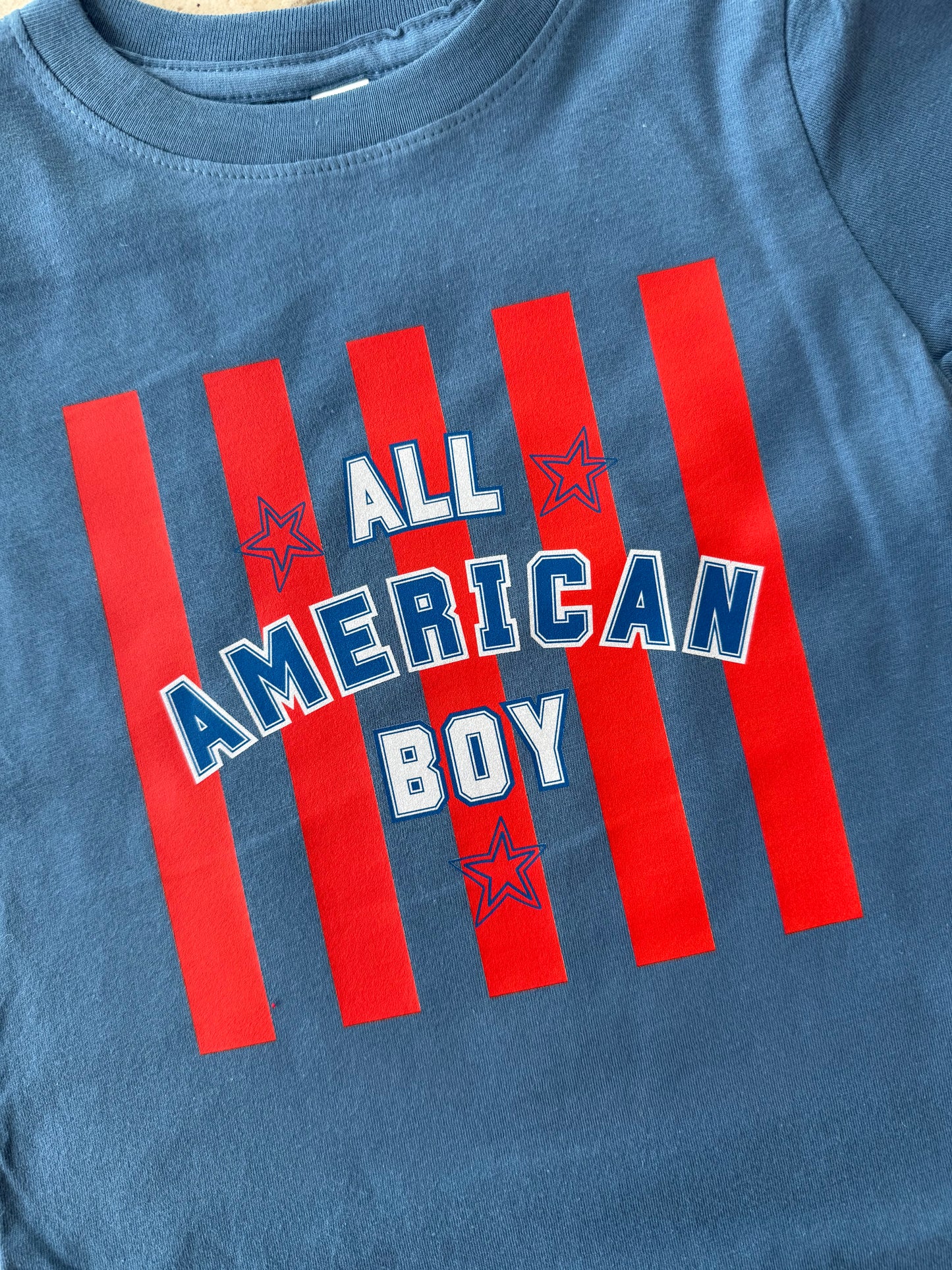 Blue t-shirt with 'All American Boy' text and red stripes on a white background
